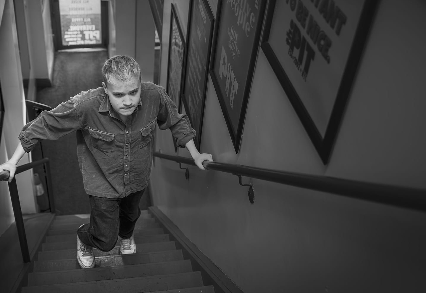 Jess, an adult man living with beck muscular dystrophy, walking up stairs to his comedy club 